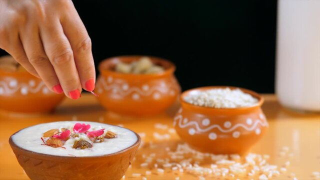 Female hand adding saffron / Kesar to a bowl of delicious rice pudding at home. Indian desserts during festival period in India - Sevai  Kheer 
