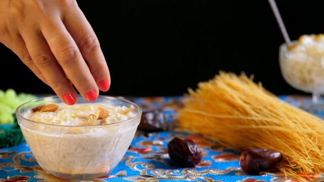 An Indian woman garnishing a bowl of tasty homemade Sevai with almonds. Raw Seviyan / vermicelli  dates for Eid feast. Festival mood  Festival celebration
