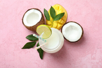Glass of tropical cocktail and ingredients on pink table