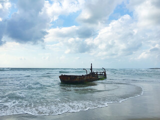 Old abandoned boat at sea at high tide against the backdrop of clouds.