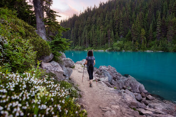 Fototapeta na wymiar Adventurous White Caucasin Adult Woman Hiking on a trail in Canadian Nature. Sunset Sky. Garibaldi Lake Hike near Whistler and Squamish, British Columbia, Canada.