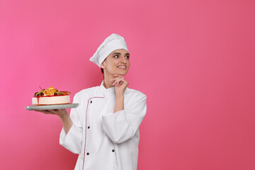 Happy professional confectioner in uniform holding delicious cake on pink background. Space for text