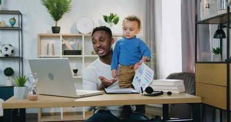Remote work and child care concept where good-looking confident loving african american holding his small son on knees during explanation of report with statistics through video chat at home - Powered by Adobe