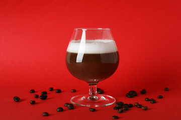 Glass of irish coffee and coffee seeds on red background