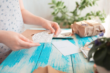 Fototapeta na wymiar A woman removing a postcard out of a craft envelope. Hands close-up. Blue wooden table with a parcel in the background. Concept of postcrossing