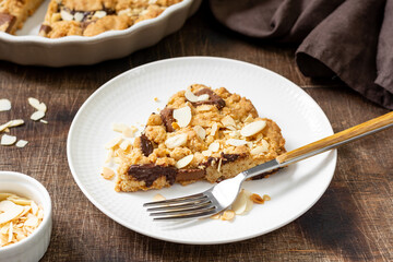 Piece of homemade shortbread pie with milk and bitter chocolate and almonds in a plate on a brown table close-up. Delicious sweet pastries