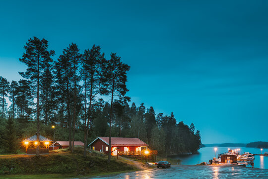 Sweden. Sweden. Beautiful Red Swedish Wooden Log Cabin House On Rocky Island Coast In Summer Night Evening. Lake Or River Landscape. Beautiful Wooden Pier Near Lake In Summer Evening Night. Lake Or