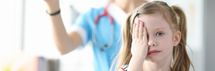 Little girl covering her eyes with her hand at ophthalmologist appointment