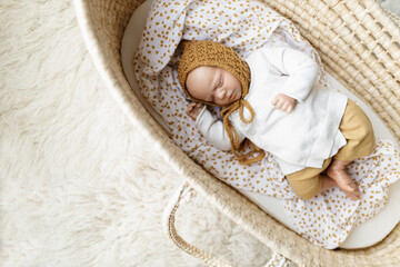 A reborn newborn baby doll toy dressed in a mustard colored bonnet hat and a white cardigan lying...