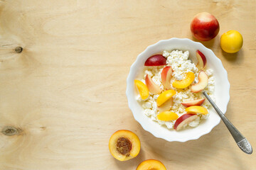 Cottage cheese with nectarine in white bowl on wooden background. Space for text