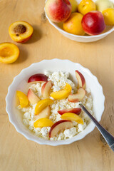 Cottage cheese with nectarine in white bowl on wooden background
