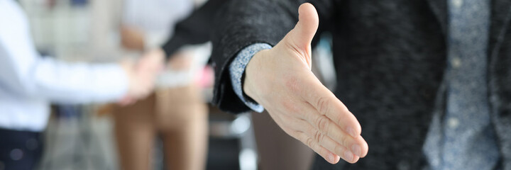 Businessman giving his hand for handshake to partner against background of colleagues closeup