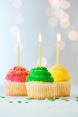 Tasty Birthday cupcakes with burning candles on table against defocused lights