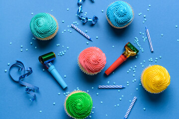 Tasty Birthday cupcakes with candles, ribbons and party whistles on color background