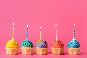 Tasty Birthday cupcakes with burning candles on color background