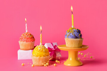 Tasty Birthday cupcakes, burning candles and gifts on color background