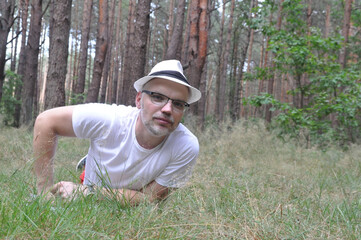 Naklejka na ściany i meble Young man in hat and forest, lying on the ground in the forest, enjoying life.