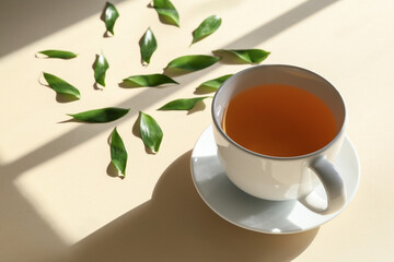 Cup of tea and green leaves on color background, closeup