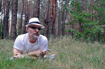 Naklejka na ściany i meble Young man in hat and forest, lying on the ground in the forest, enjoying life.