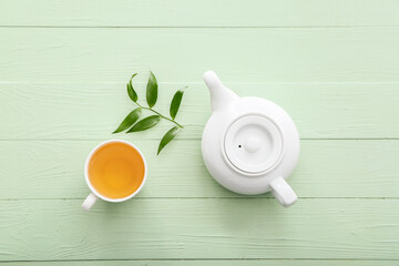 Teapot and cup of tea with green leaves on color wooden background