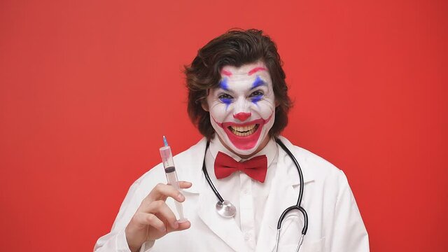 The male clown doctor prepared a syringe, highlighted on a red background, intending to treat someone. Phobia of doctors, sleep