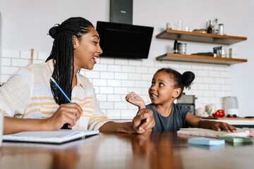 Black woman and her daughter smiling and writing in exercise books