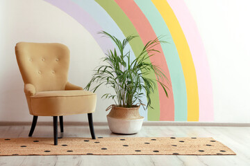 Comfortable chair, runner rug and houseplant near white wall with rainbow art indoors