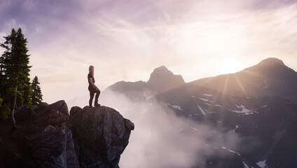 Fantasy Adventure Composite with a Woman on top of a Mountain Cliff with Dramatic Nature Scenery. Sunset or Sunrise Sky. Aerial Background Landscape from British Columbia, Canada.