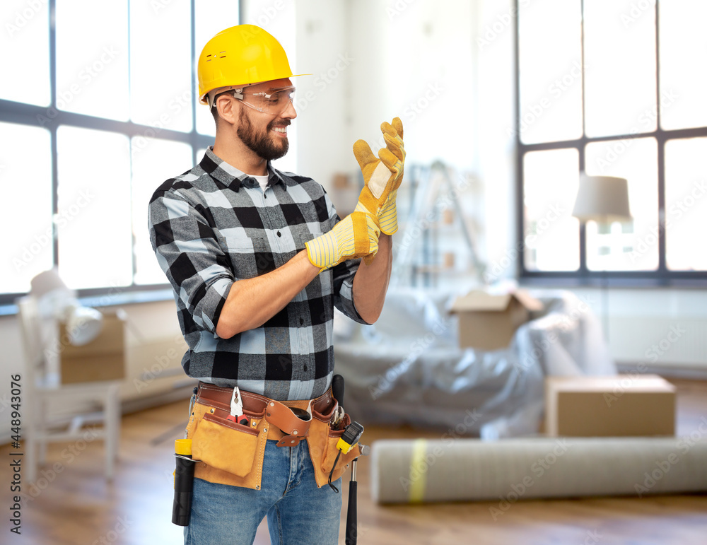 Wall mural repair, construction and building concept - happy smiling male worker or builder in helmet and gloves over home room background