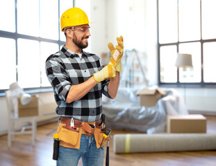 repair, construction and building concept - happy smiling male worker or builder in helmet and gloves over home room background