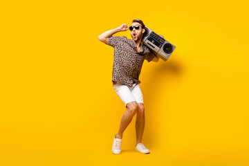 Full length photo of cool excited gentleman dressed print shirt arm dark glasses dancing boombox isolated yellow color background