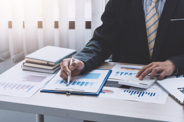 Close-up of a businessman hand holding a pen pointing at a graph using a calculator to calculate at the office.