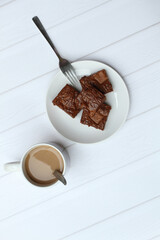 Top view of chocolate brownies and on a white plate and a glass of latte on white cafe table