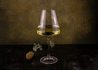 a glass of white wine with small chamomile inflorescences and a cork