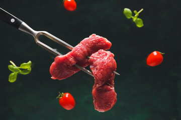 Carving fork with raw beef meat slices on dark background