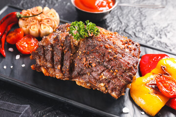Board with tasty beef brisket and grilled vegetables on dark background