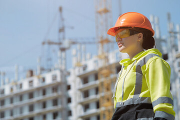 An engineer in a green hoodie with reflective ribbons and a construction control helmet conducts an inspection while inspecting the construction site