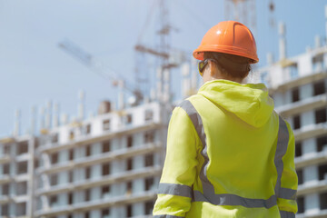 An engineer in a green construction hoodie and helmet manages the construction process by inspecting the construction process