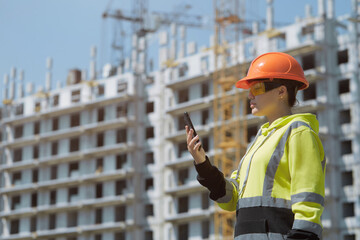 A young engineer girl sends messages on her phone controlling the construction process, with a multi-storey building under construction in the background