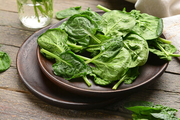 Plate with fresh spinach leaves on wooden background, closeup