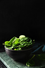 Bowl with fresh spinach leaves on dark background