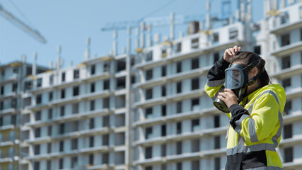 An employee of the gas and environmental inspection puts on a gas mask against the background of an industrial unfinished building