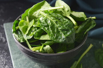 Bowl with fresh spinach leaves on dark background, closeup