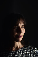 Portrait of a beautiful woman in her fifties wearing a black blouse with white diamonds on a black background having a serious look vertically