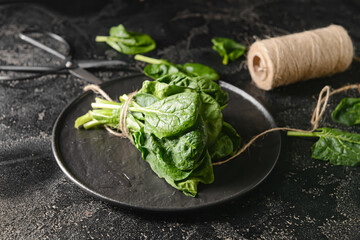 Plate with fresh spinach leaves, scissors and threads on dark background