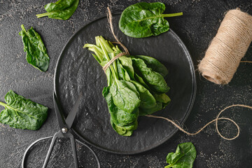 Plate with fresh spinach leaves, scissors and threads on dark background