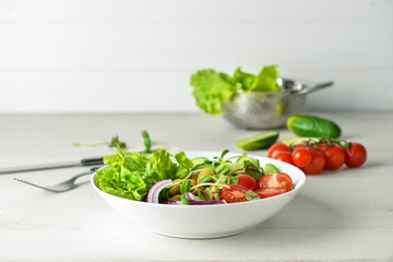 Bowl of fresh salad with vegetables on white wooden background