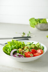 Bowl of delicious fresh salad with vegetables on white wooden table