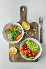 Wooden board with bowls of delicious vegetable salad on light background