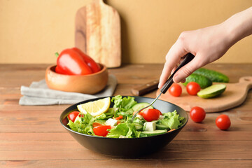 Woman eating tasty fresh salad with vegetables and feta cheese on light background